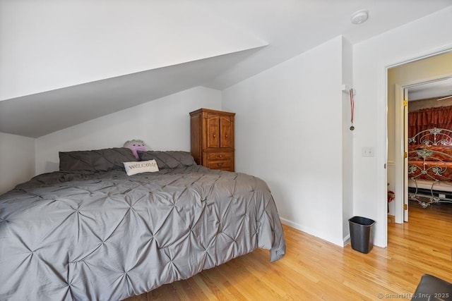 bedroom with vaulted ceiling, wood finished floors, and baseboards