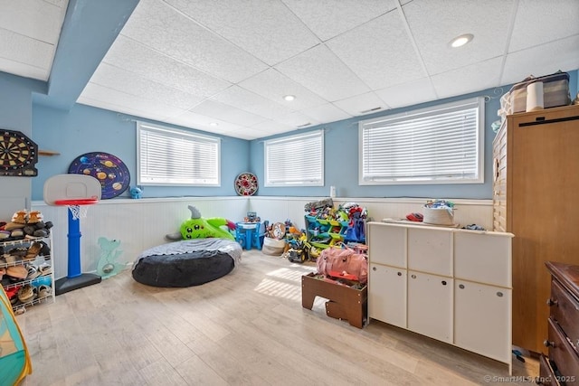 rec room with light wood finished floors, wainscoting, and a paneled ceiling