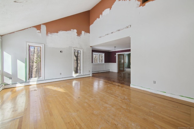 unfurnished living room with vaulted ceiling, baseboard heating, wainscoting, and wood finished floors