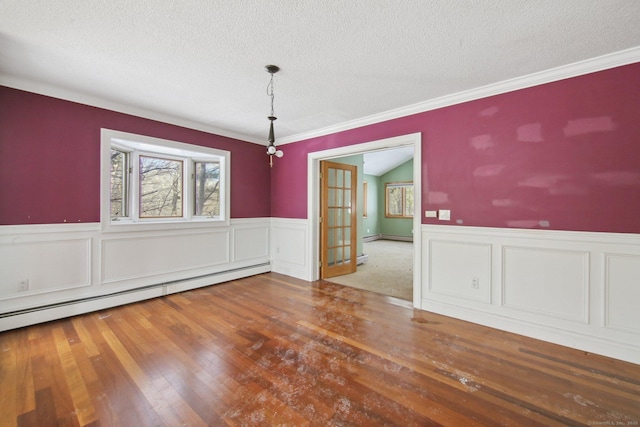 unfurnished dining area with a baseboard heating unit, a textured ceiling, wainscoting, and wood finished floors