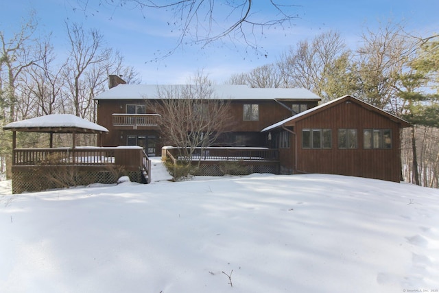 snow covered rear of property with a chimney and a wooden deck