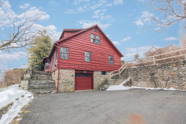 view of front of house featuring a garage, stone siding, stairs, and aphalt driveway