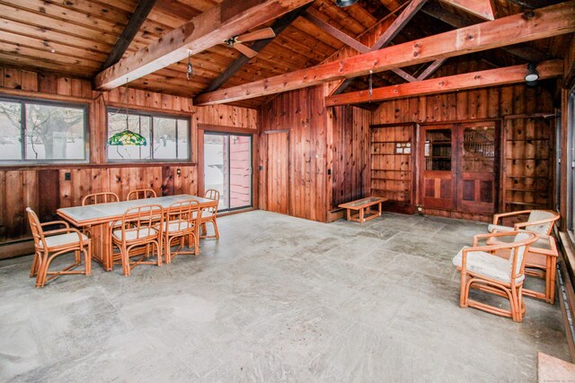 dining space with lofted ceiling with beams, wood ceiling, wooden walls, and concrete flooring