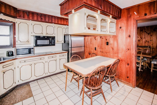 kitchen featuring light tile patterned floors, light countertops, appliances with stainless steel finishes, wood walls, and a sink