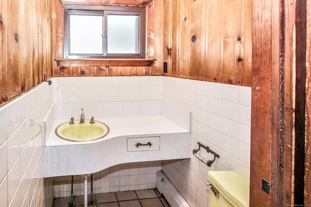 bathroom featuring wooden walls, toilet, a sink, tile patterned flooring, and tile walls