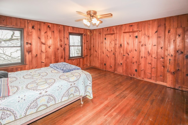 bedroom with wood-type flooring, wooden walls, and a ceiling fan