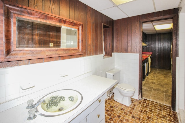 bathroom featuring a paneled ceiling, vanity, toilet, and wooden walls