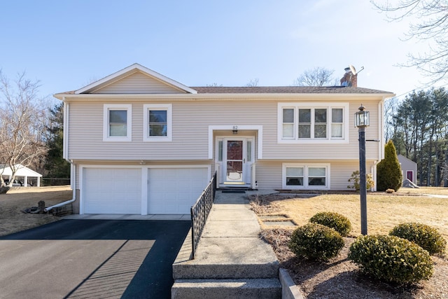 split foyer home featuring driveway, a chimney, and an attached garage