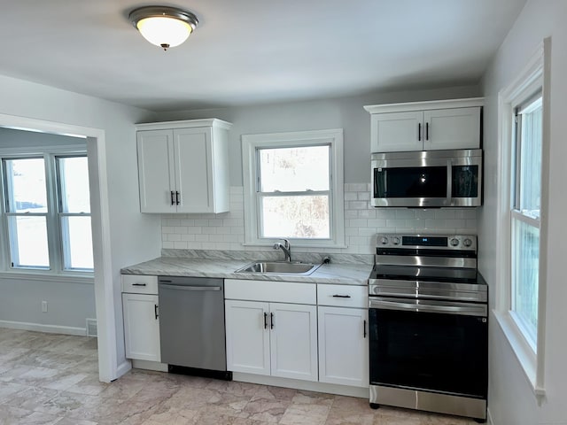 kitchen with sink, appliances with stainless steel finishes, light stone countertops, white cabinets, and decorative backsplash