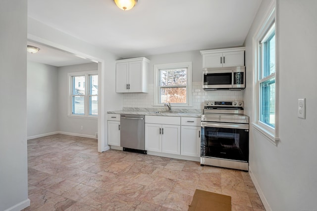 kitchen featuring tasteful backsplash, appliances with stainless steel finishes, white cabinetry, a sink, and baseboards