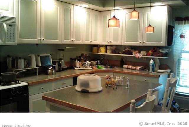 kitchen featuring sink, decorative light fixtures, range with gas cooktop, and white cabinets