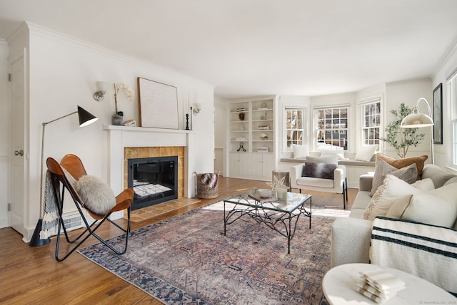 living room featuring hardwood / wood-style floors, a tiled fireplace, and crown molding