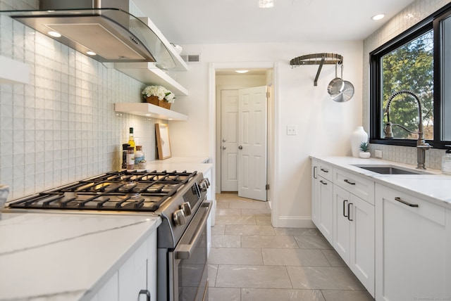 kitchen with exhaust hood, light stone countertops, white cabinets, stainless steel gas stove, and sink