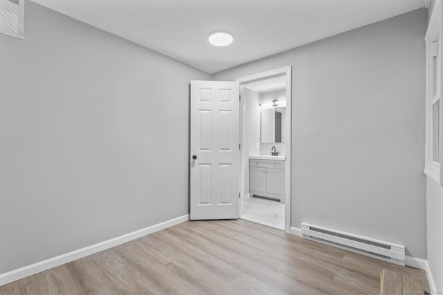 spare room featuring a baseboard heating unit, sink, and light wood-type flooring