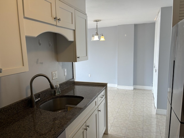 kitchen with hanging light fixtures, dark stone counters, refrigerator, light tile patterned floors, and sink