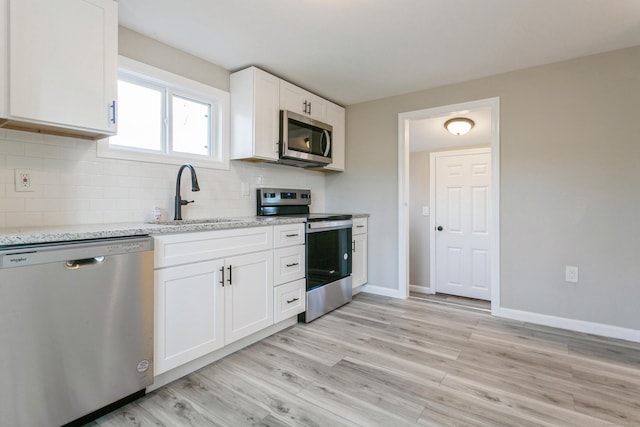 kitchen with appliances with stainless steel finishes, tasteful backsplash, white cabinetry, sink, and light stone counters