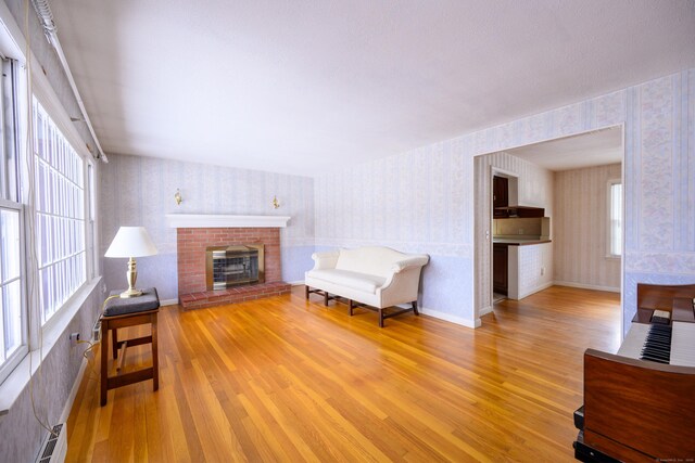 living area with wood finished floors, a brick fireplace, and wallpapered walls