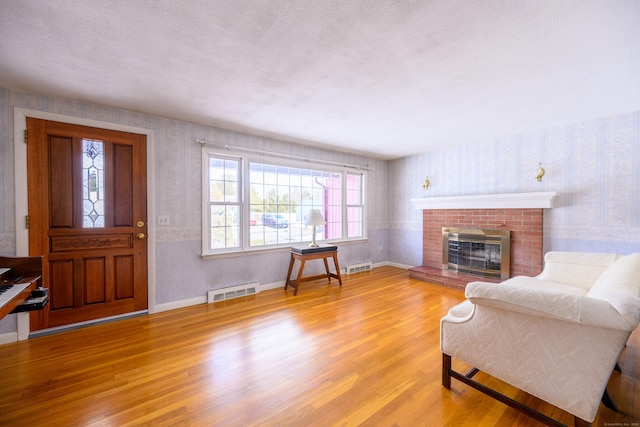 living area featuring a textured ceiling, a fireplace, visible vents, light wood finished floors, and wallpapered walls