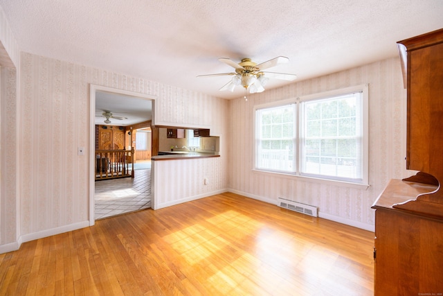 unfurnished living room with visible vents, light wood-style flooring, a textured ceiling, and wallpapered walls