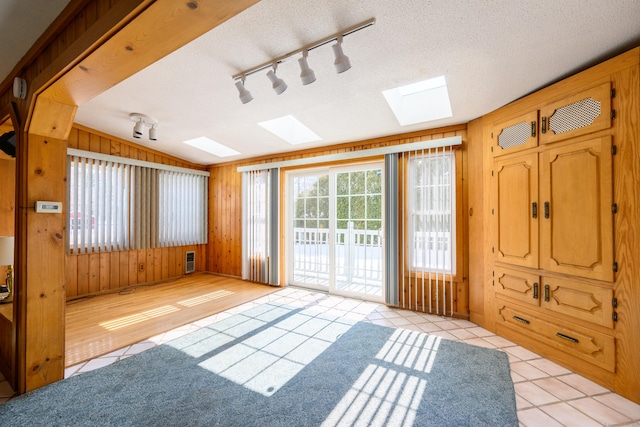 spare room featuring lofted ceiling with skylight, light tile patterned flooring, wooden walls, and a textured ceiling