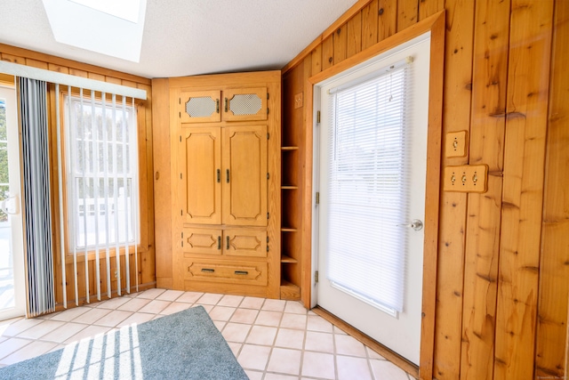 doorway featuring light tile patterned floors, wood walls, a skylight, and built in features