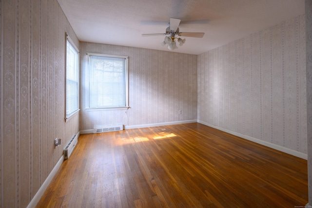 unfurnished room featuring a baseboard heating unit, wood-type flooring, visible vents, and wallpapered walls