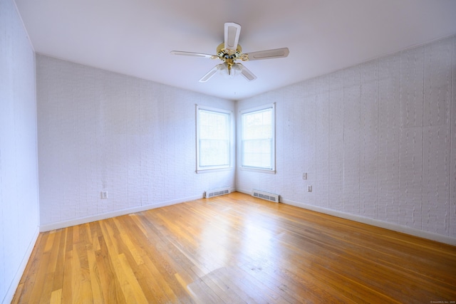 empty room featuring brick wall, wood finished floors, and visible vents