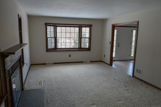 unfurnished living room featuring a healthy amount of sunlight, visible vents, and light colored carpet