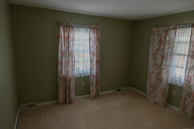 empty room featuring a wealth of natural light, visible vents, and light colored carpet