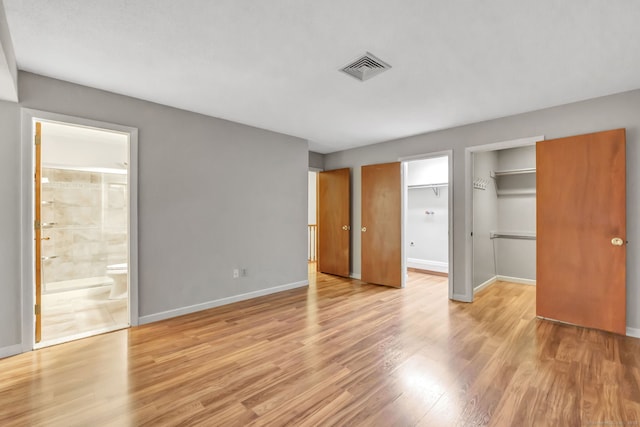 unfurnished bedroom with light wood-type flooring, connected bathroom, and a spacious closet