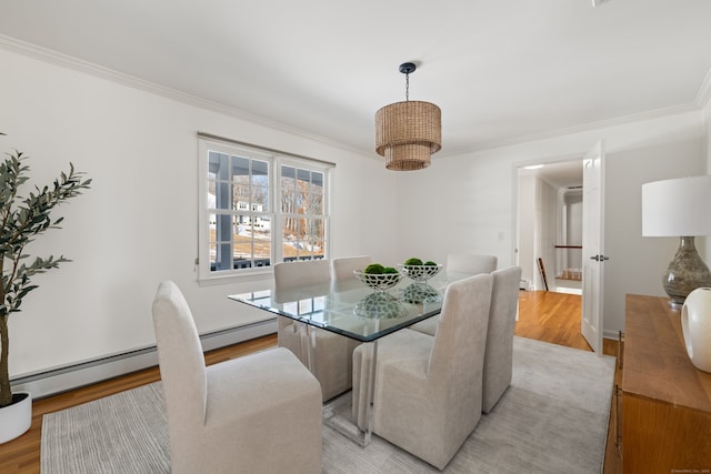 dining space featuring a baseboard heating unit, ornamental molding, and light wood-type flooring