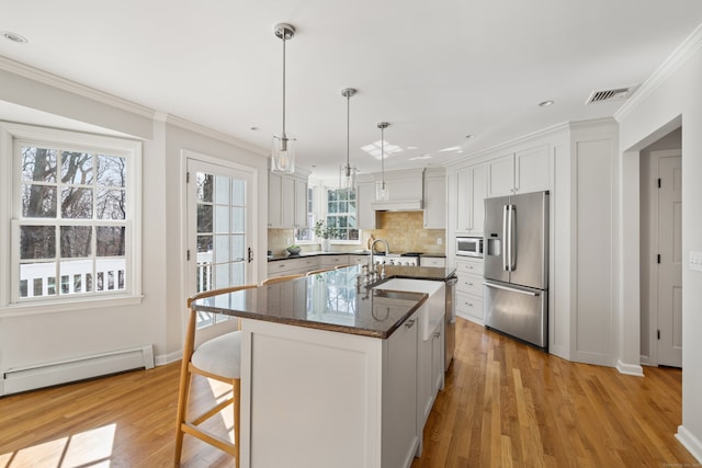 kitchen with a kitchen island with sink, a baseboard heating unit, white cabinetry, stainless steel refrigerator with ice dispenser, and dark stone countertops