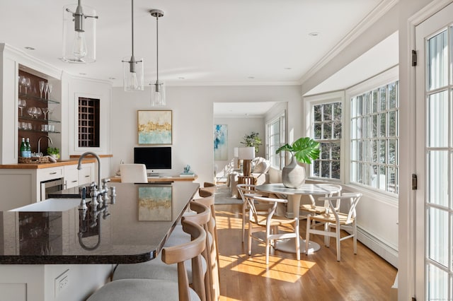 dining space with light wood finished floors, ornamental molding, baseboard heating, and indoor wet bar