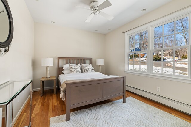 bedroom featuring light wood-type flooring, a baseboard radiator, baseboards, and a ceiling fan