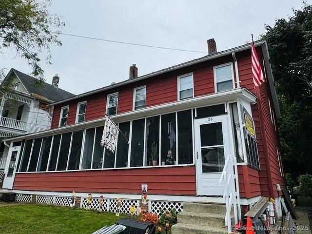 rear view of house with a sunroom, a chimney, and a yard