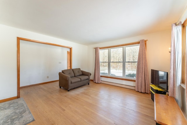 living area with a baseboard radiator, baseboards, and light wood-style floors