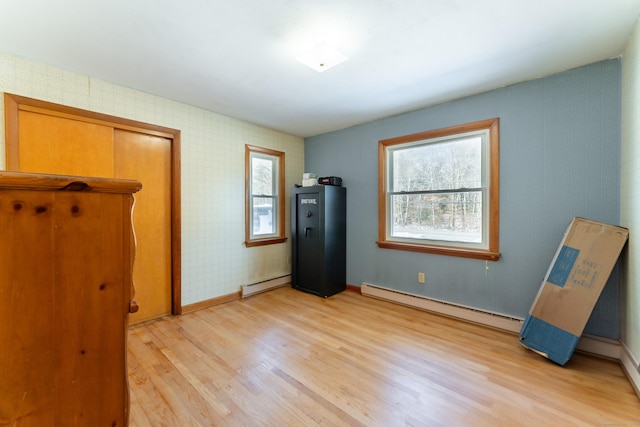 unfurnished bedroom featuring light wood-style flooring, wallpapered walls, a baseboard radiator, baseboards, and baseboard heating