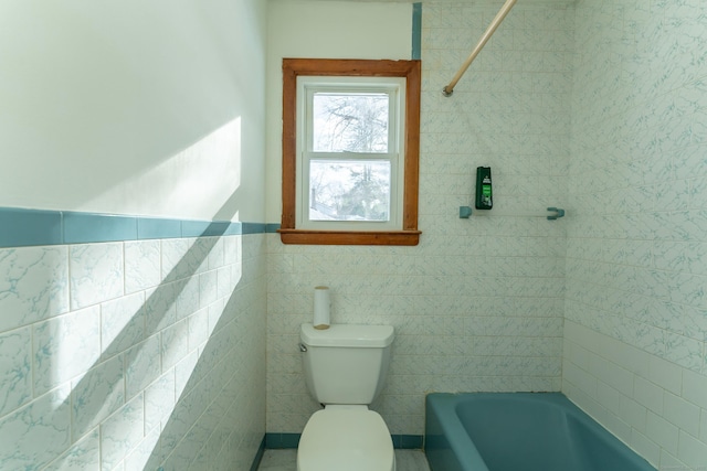 bathroom with tile walls, toilet, and a wainscoted wall