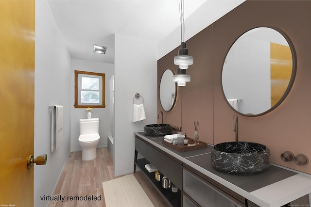 full bath featuring toilet, a sink, wood finished floors, double vanity, and baseboards