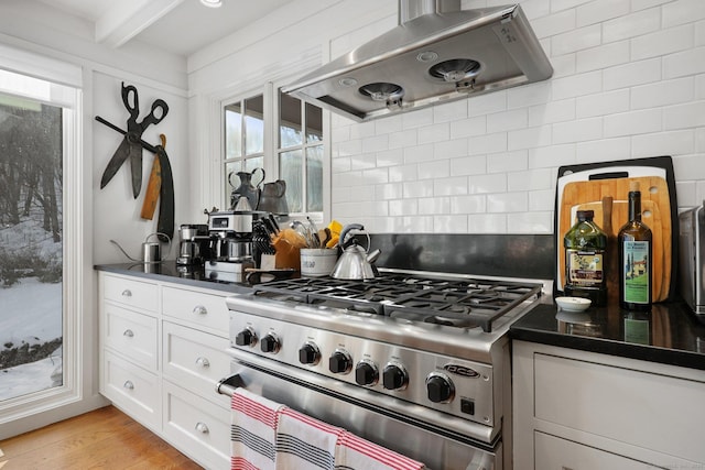 kitchen with dark countertops, wall chimney range hood, gas stove, and decorative backsplash