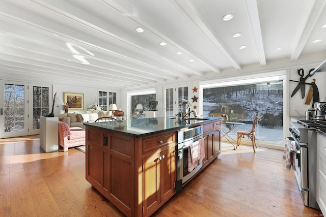 kitchen with french doors, brown cabinets, a center island with sink, light wood-style flooring, and appliances with stainless steel finishes