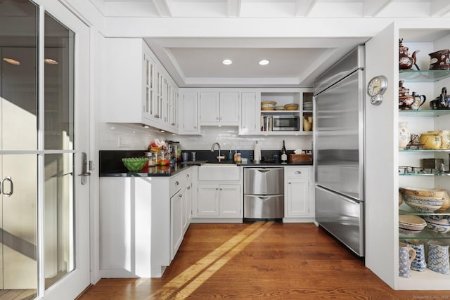 kitchen with dark wood finished floors, open shelves, dark countertops, a sink, and built in appliances