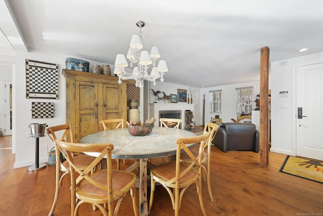 dining room with light wood finished floors, a warm lit fireplace, a chandelier, and baseboards