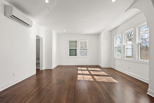 empty room featuring an AC wall unit, dark wood-style flooring, recessed lighting, and baseboards