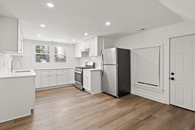 kitchen with stainless steel appliances, visible vents, light wood-style floors, a sink, and under cabinet range hood