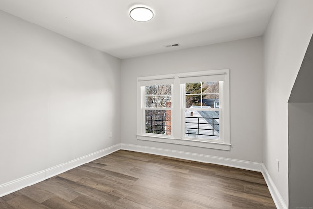 unfurnished room featuring dark wood-type flooring, visible vents, and baseboards