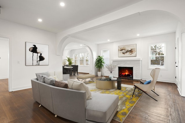 living area with baseboards, arched walkways, dark wood-type flooring, a fireplace, and recessed lighting