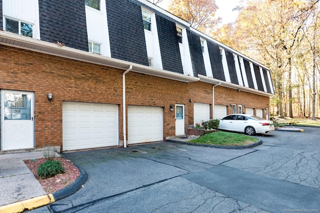 exterior space featuring a shingled roof, brick siding, an attached garage, and mansard roof