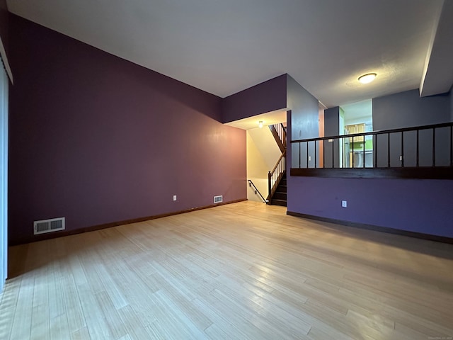 unfurnished room with light wood-style floors, visible vents, stairway, and baseboards