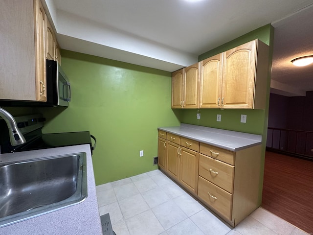 kitchen featuring light tile patterned floors, light countertops, stainless steel microwave, light brown cabinetry, and a sink